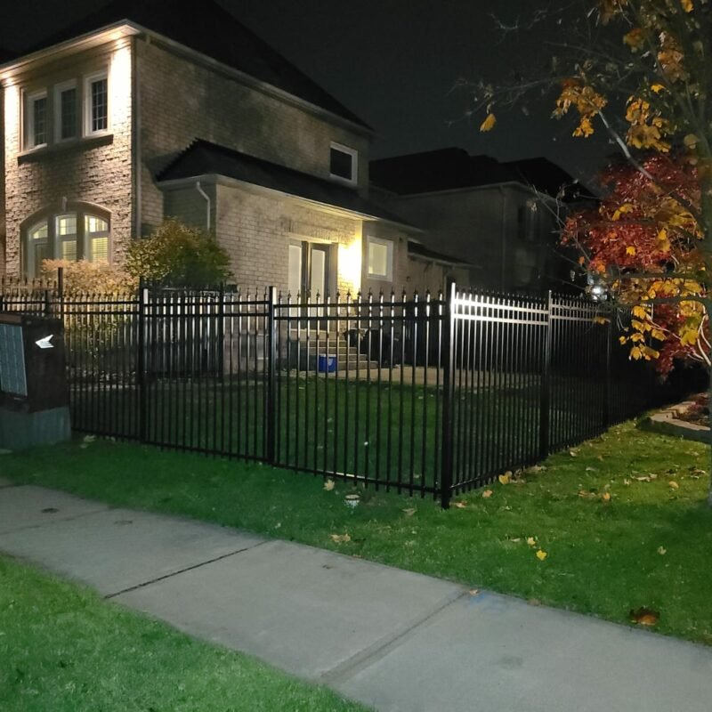 Residential black aluminum picket fence at night