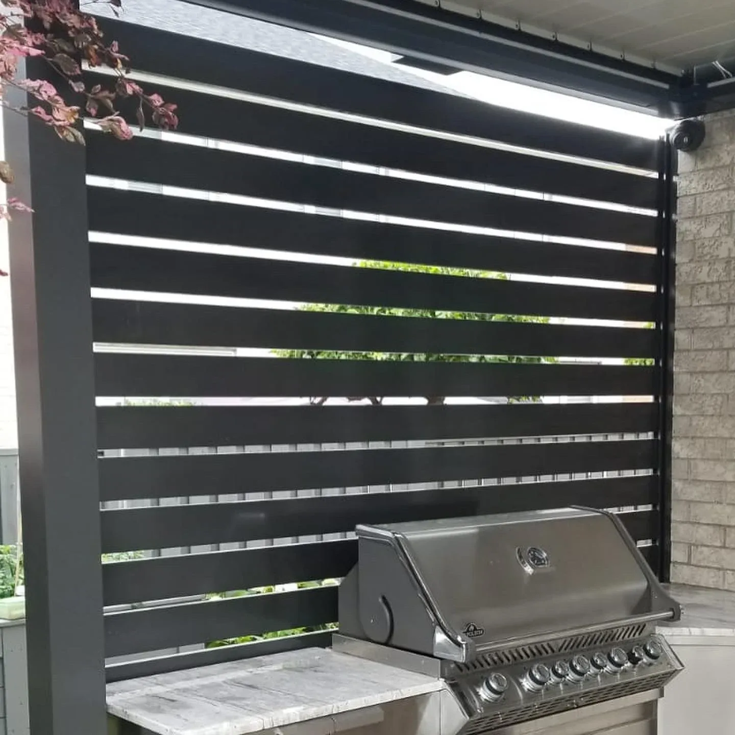 Black aluminum horizontal slat privacy fence behind outdoor kitchen and barbecue