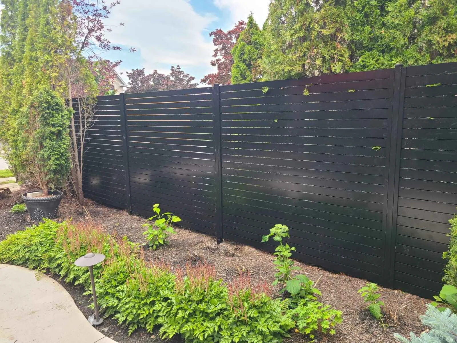Black aluminum horizontal slat fence panels along a landscaped garden