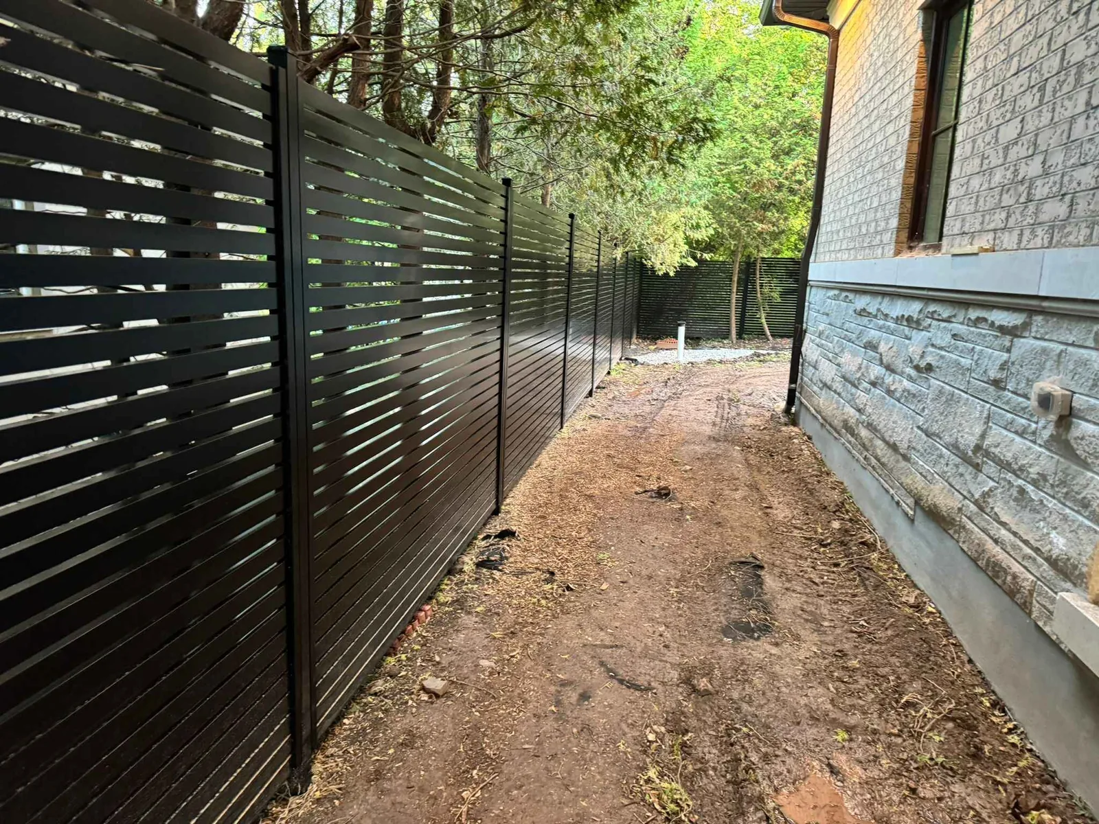 Long black aluminum horizontal slat fence installed along side yard beside house